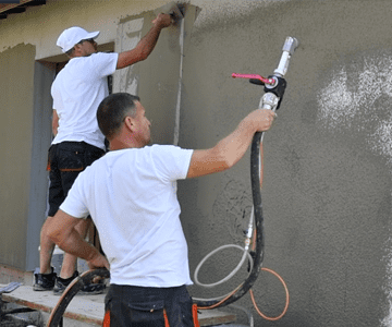 Двама мъже предоставят ремонтни Услуги чрез пръскане на стена с маркуч.