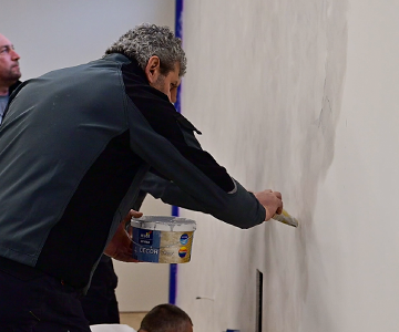 Мъж използва ремонтни услуги за боядисване на стена с четка.
