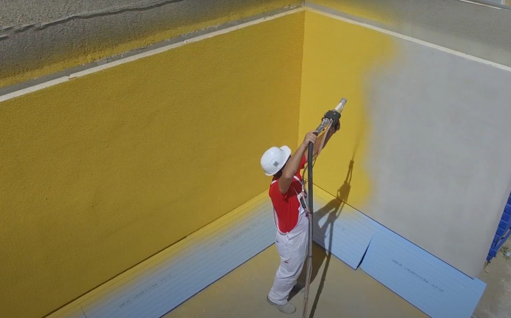 Човек пръска жълта боя върху стена.